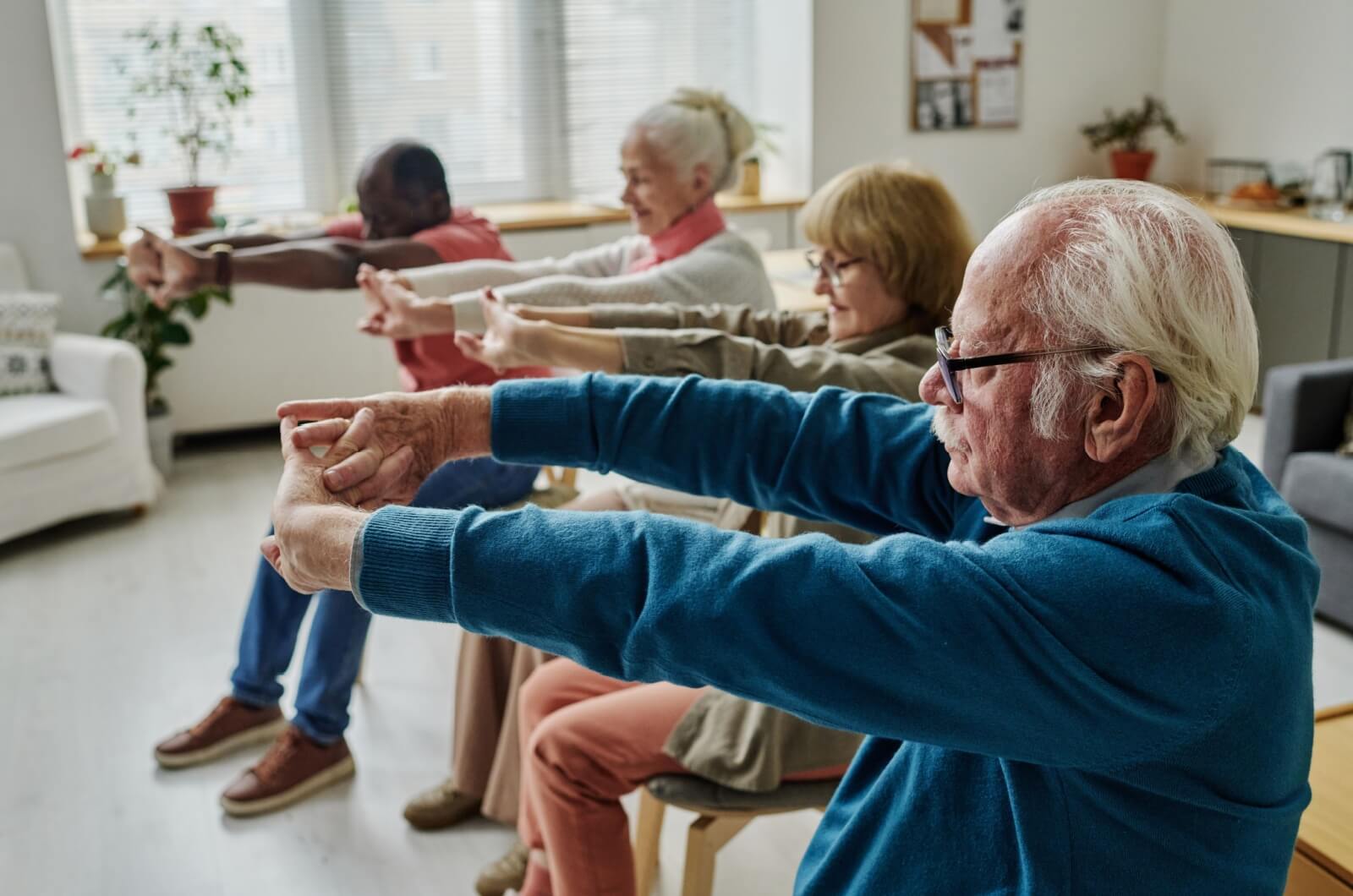 Older adults in memory care exercising while seated in chairs.