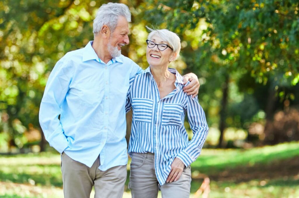 An older married couple walking through a park with arms around one another on a day trip to Orlando.