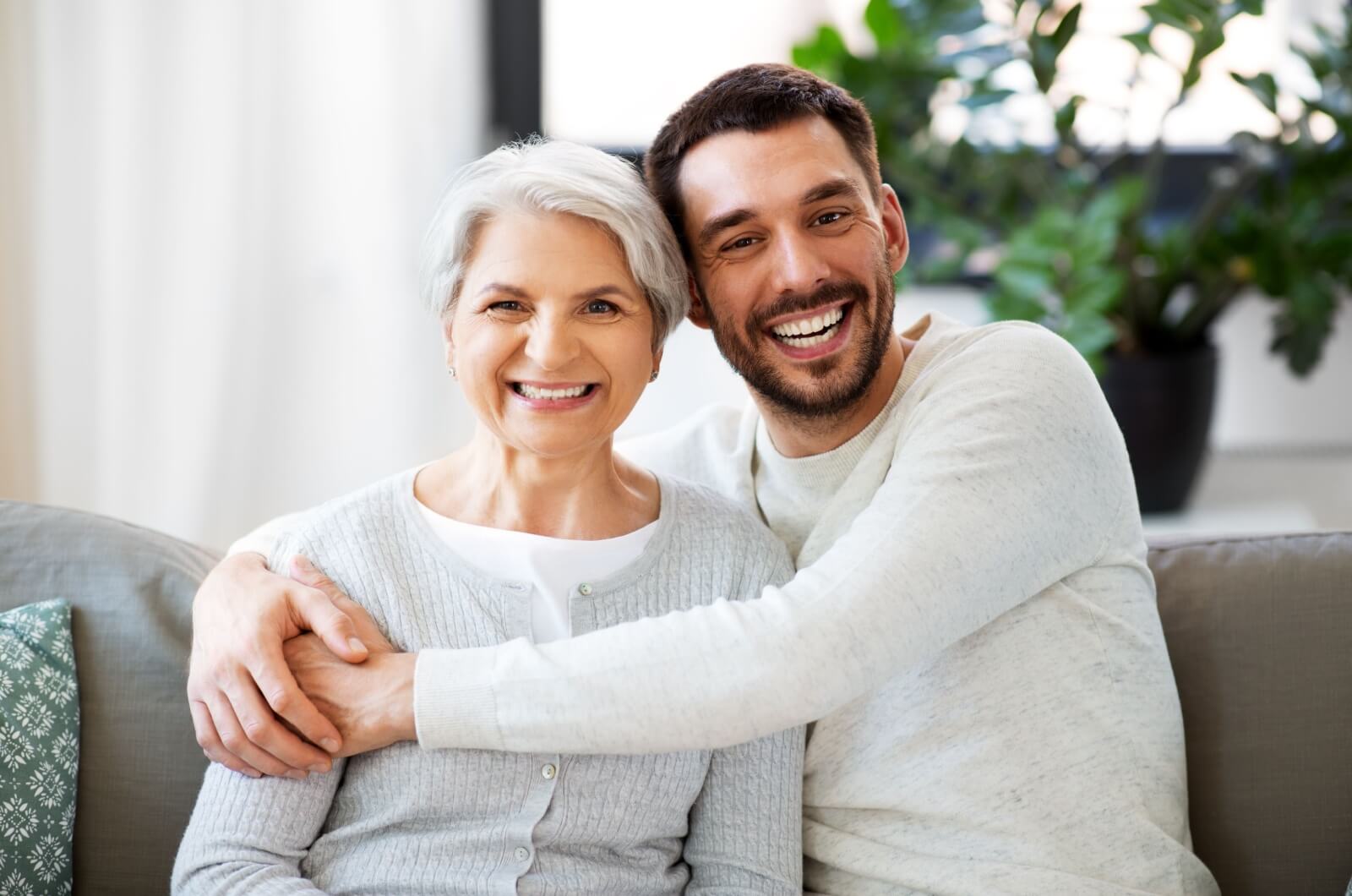 A smiling adult man hugs his older, smiling mother.