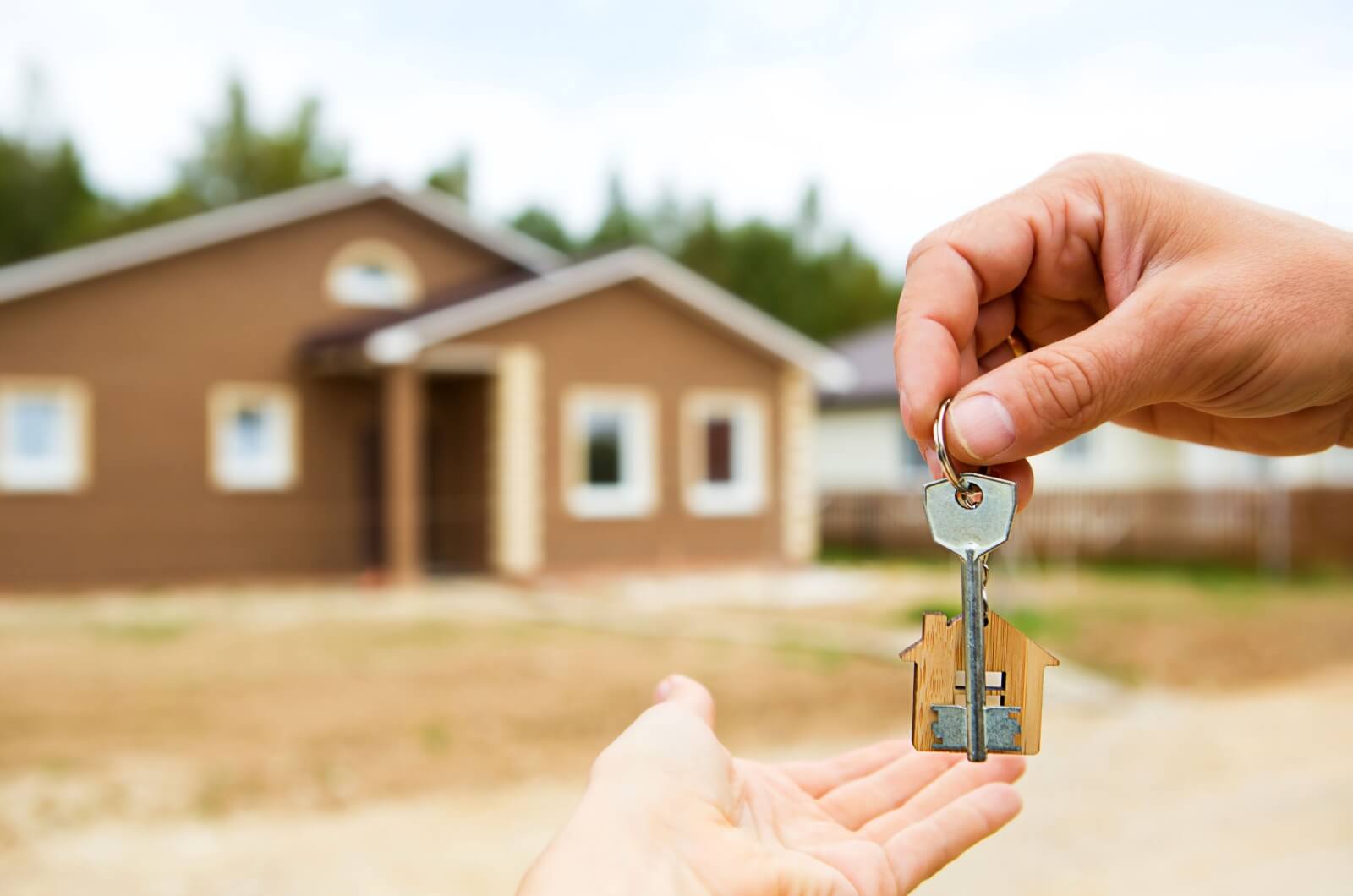 A hand extends, passing a key to the new homeowner with a gesture of transfer and ownership