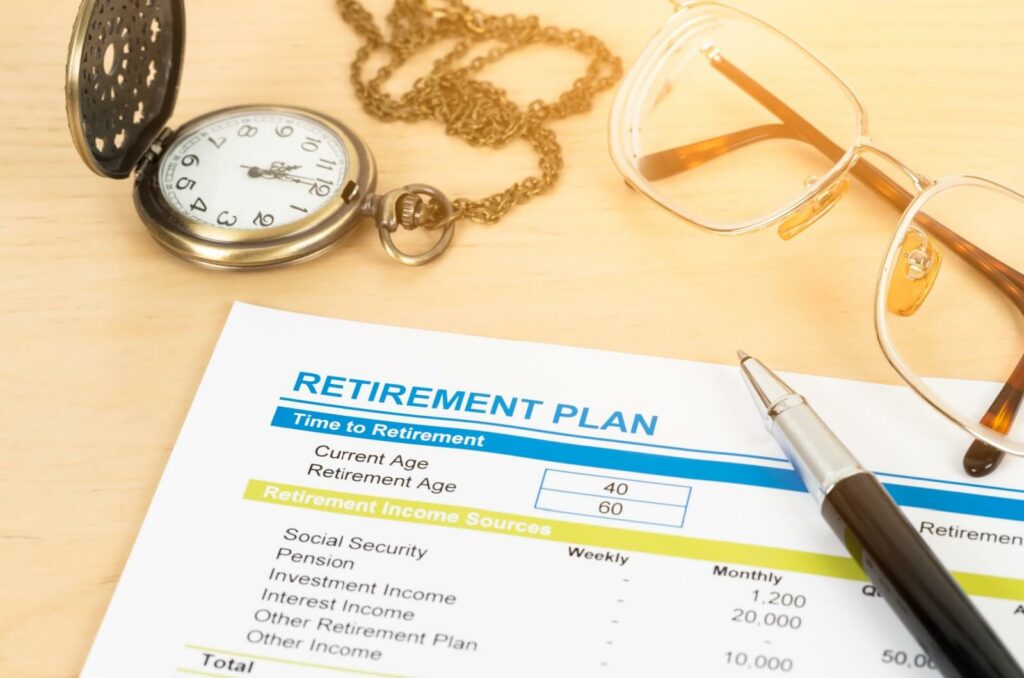 On the table, there sits a retirement plan document alongside a ballpoint pen, pocket watch and an eyeglasses