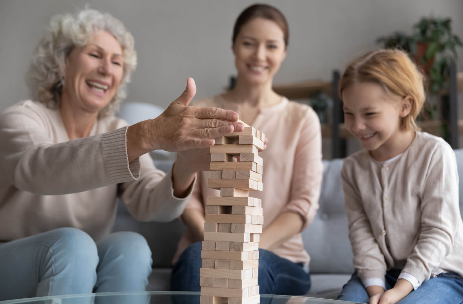 An adult with their young child visiting their older parent in memory care, laughing together and playing an engaging game of Jenga.