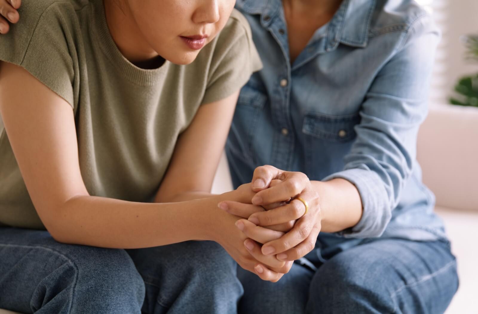 Adult child sitting on a couch with their older parent and feeling stressed about caring for them.