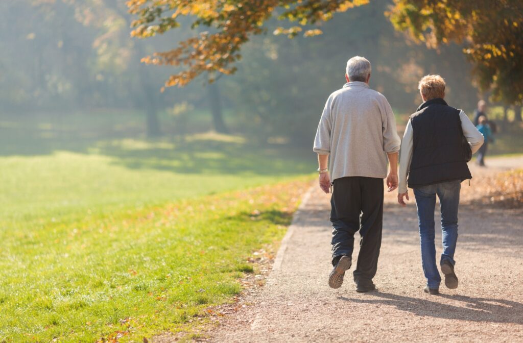 A behind view of an older couple walking on a path in a park on a sunny day.