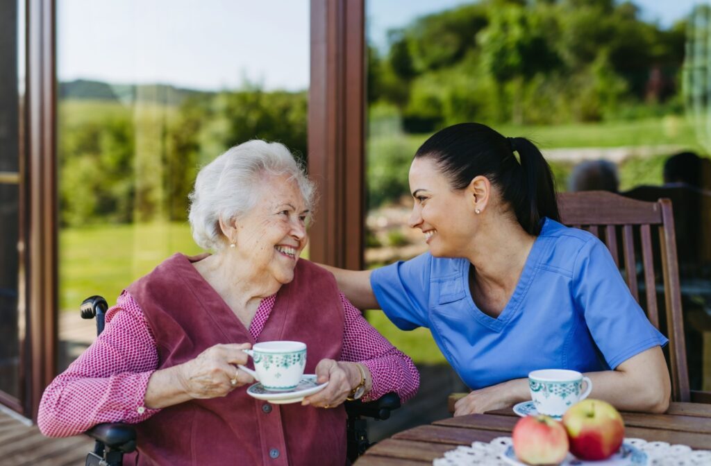 An older adult having tea and smiling at a staff member in senior living.