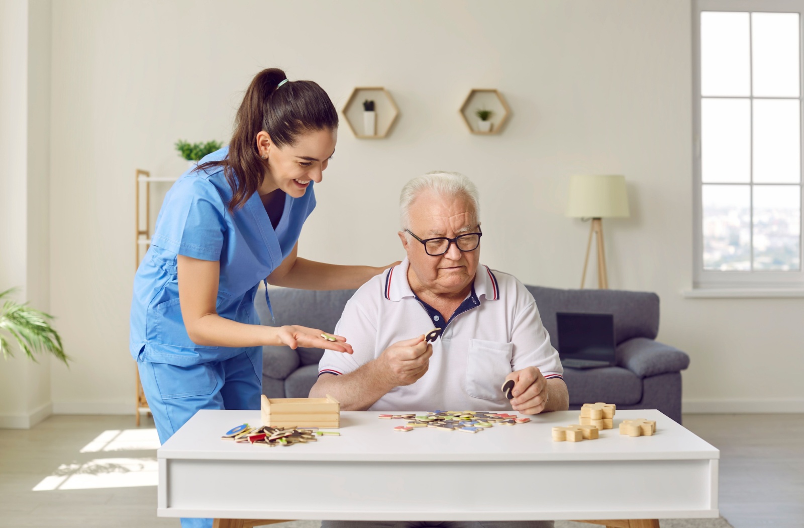 A smiling caregiver helps an older adult do a puzzle.