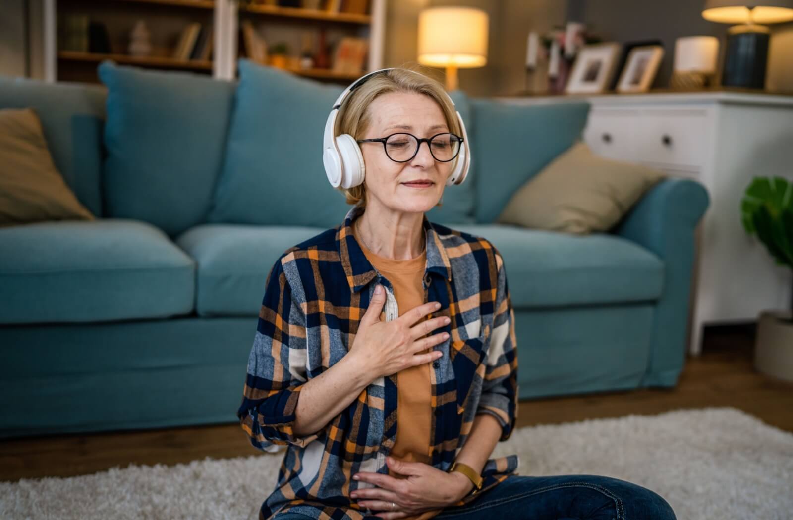 A senior relaxes with one hand on their chest and stomach, eyes closed, listening to music, and breathing