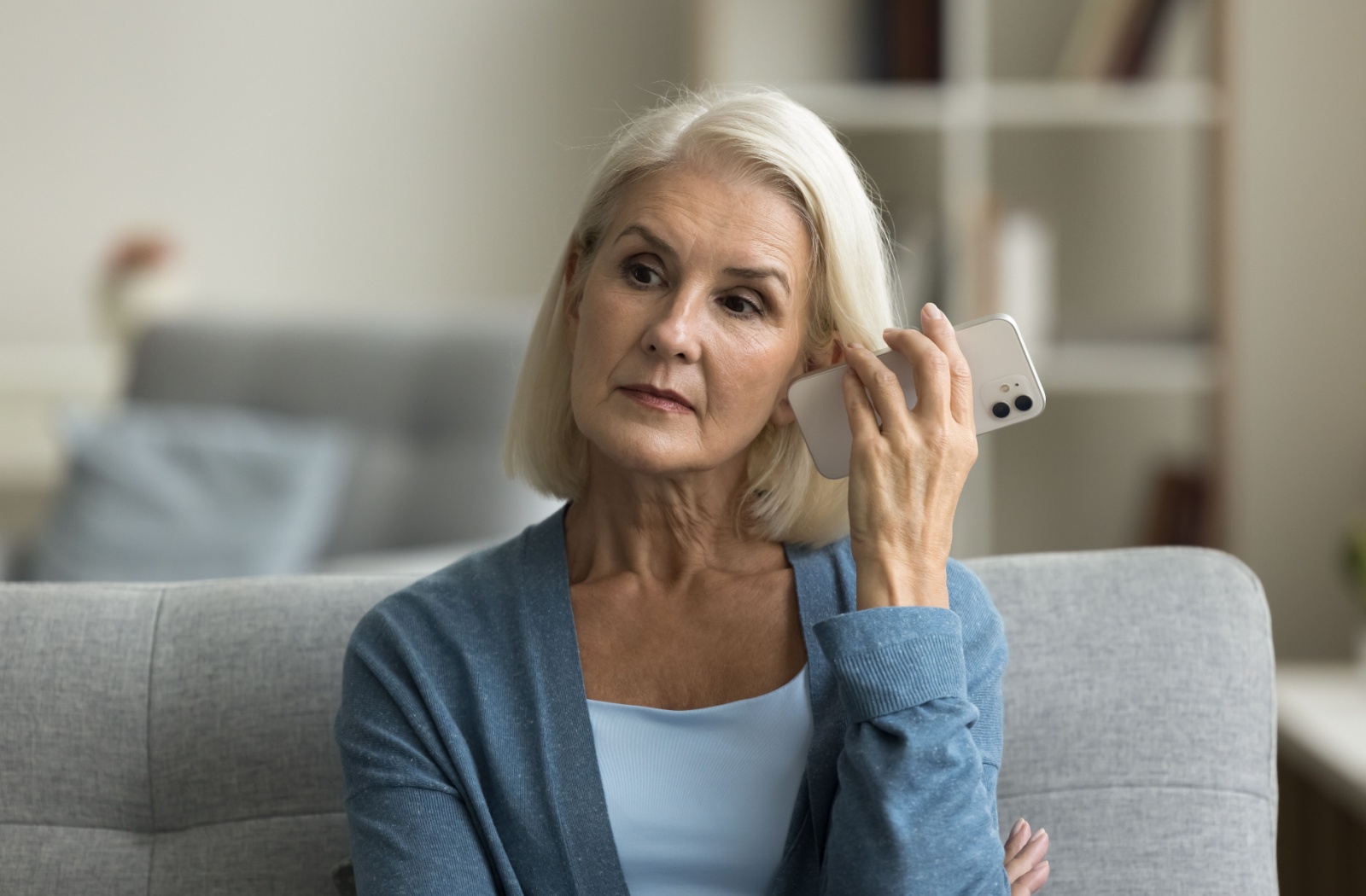 A senior calmly listens to a weather report on their phone.